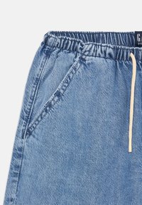 Bermudas de denim azul claro con cintura elástica y cordón crema. Cuenta con bolsillos laterales y una tela texturizada con detalles de costura.