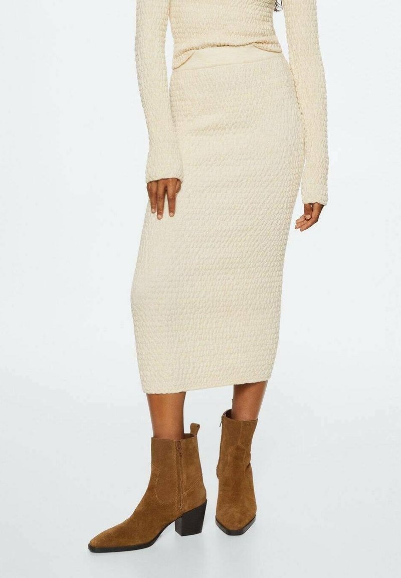 Světlý krémový midi sukňový model s texturou a přiléhavým střihem, doplněný hnědými semišovými kotníkovými botami na blokovém podpatku a bočním zipem.