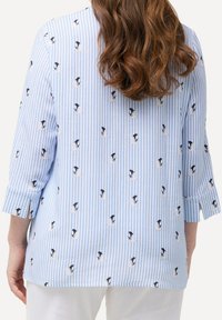 Chemise bleu clair avec des rayures verticales blanches, ornée d'un motif de petits pingouins. Manches trois-quarts et coupe ample. Texture de tissu douce.