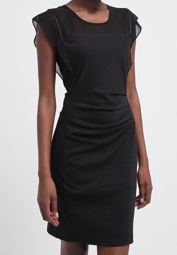 Femme portant une robe noire ajustée longueur genou avec des manches courtes transparentes et un panneau supérieur transparent au niveau de la poitrine.