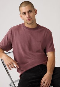 Μπορντό βαμβακερό κοντομάνικο T-shirt με στρογγυλή λαιμόκοψη και διακριτική λεπτομέρεια λογότυπου στο στήθος, σε συνδυασμό με μαύρο τζιν. Λείο ύφασμα, άνετη εφαρμογή.