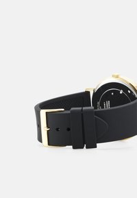 Schwarzes Silikon-Uhrenarmband mit einer goldenen Edelstahl-Schnalle. Rundes schwarzes Zifferblatt auf der Rückseite sichtbar mit strukturiertem Oberfläche.