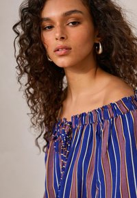 Top scollato sulle spalle, a righe blu e viola con scollatura arricciata e dettaglio con fiocco. Tessuto morbido con righe verticali in evidenza.