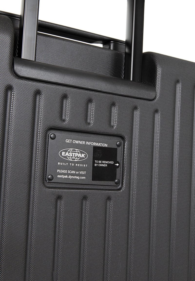 Valise rigide noire avec surface texturée. Équipée d'une poignée rétractable et d'une étiquette pour les informations du propriétaire, portant la mention "EASTPAK."