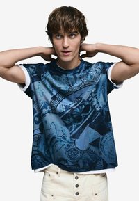 Modré grafické tričko s krátkymi rukávmi, zdobené zložitými vzormi a dizajnmi, s pevným bielym okrúhlym výstrihom a textúrovanou tkaninou.