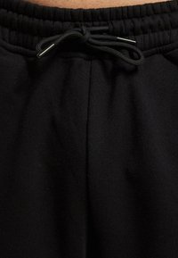 Pantaloni de trening negri dintr-un material texturat, cu talie elastică și șnur ajustabil. Prezintă cusături pe laturile din față pentru un aspect ajustat.