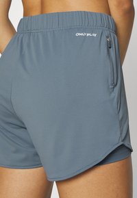 Ljusblå sportshorts med en texturerad tygstruktur, med midjeband i elastisk resår och en ficka med dragkedja på sidan. Logotypen för märket finns på midjebandet.