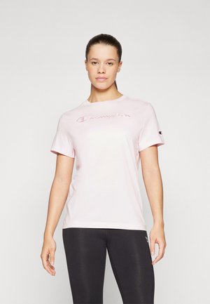 Camiseta de manga corta rosa, hecha de algodón suave, con un destacado logo bordado de "Champion" en el pecho. Cuello redondo simple.