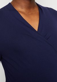 Marinblå omslagstopp i mjukt material, med V-ringning och slät textur samt rynkdetaljer på ena sidan.