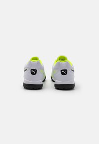 Zapatillas deportivas blancas con acentos reflectantes, logo negro y lengüeta trasera de neón amarillo. Parte superior de malla texturizada y suela de goma negra.
