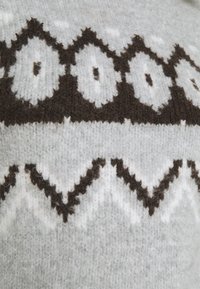 Tissu en tricot gris avec un motif géométrique présentant des formes marron foncé et blanches. Fini texturé avec des accents en zigzag.
