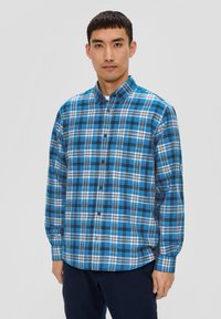 Chemise à carreaux bleus et noirs à manches longues, avec un col à boutons et des accents blancs. Fabriquée en tissu doux et texturé.