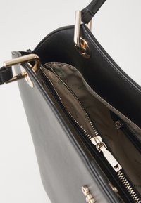 Sort syntetisk håndtaske med guldfarvet hardware, lynlåslommer og en glat tekstur. Indvendigt har den beige foring med logo print.