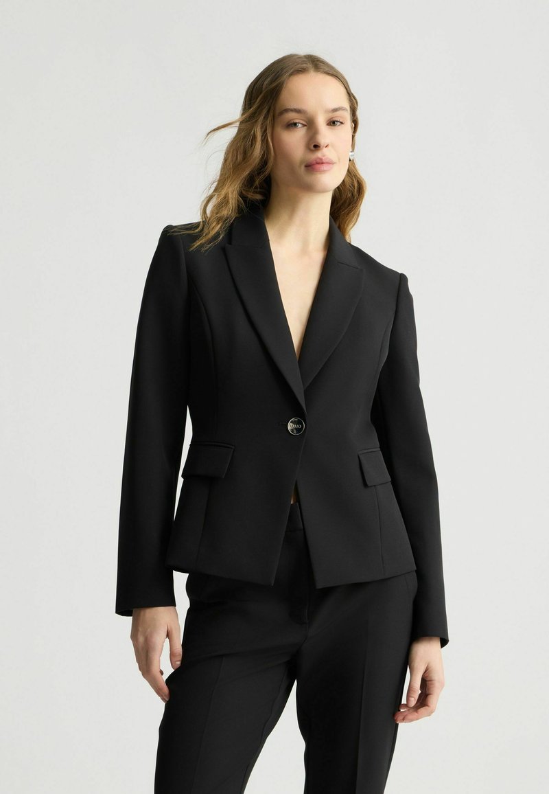 Blazer nero con vestibilità su misura, dotato di chiusura a un bottone, rever a punta e due tasche frontali. Tessuto liscio e design strutturato.