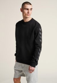 Sudadera negra de manga larga con accents en forma de chevron gris texturizado a lo largo de las mangas, fabricada en un tejido suave, con un escote de tipo barco.