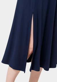 Abito blu navy con spacchi laterali, realizzato in tessuto morbido. Presenta un design fluido e un orlo che arriva a metà polpaccio, con una texture liscia.