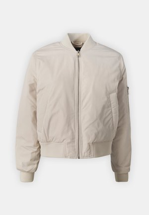 Világos bézs bomber dzseki elülső cipzárral, két oldalsó zsebbel, bordázott mandzsettával és bordázott derékkal. Simára fényezett anyag, minimális designnal.