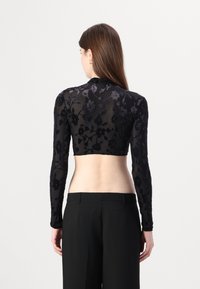 Svart langermet crop topp laget av tynt stoff, med blomsterbroderi. Designet har høy krage og tettsittende ermer.