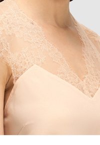 Vaaleanpunainen mekko, jossa on v-aukko, satiinikangas ja läpinäkyvä pitsireunus hartioilla, luoden hienostuneen, tekstuurisen yksityiskohdan.