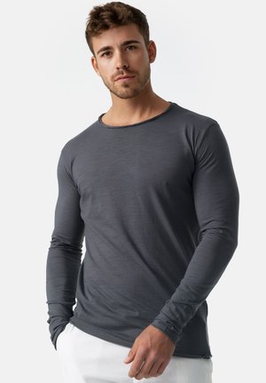 Chemise grise à manches longues, en tissu doux, col rond, design ajusté, texture subtile, détails de couture minimalistes, associée à un pantalon blanc.