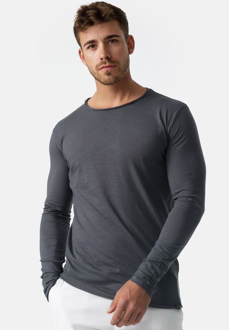 Camisa gris de manga larga, con tejido suave, cuello redondo, diseño ajustado, textura sutil, detalles de costura mínimos, combinada con pantalones blancos.