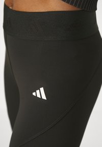 Leggings neri con un ampio elastico nero in vita che presenta un motivo testurizzato. Un logo triangolare bianco è visibile sulla parte bassa della gamba.