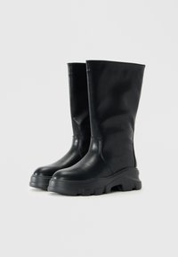 Ein Paar schwarze Lederstiefel bis zur Wade mit klobigen Profilsohlen, runden Zehen und glatter Textur, vor einem schlichten weißen Hintergrund gezeigt.