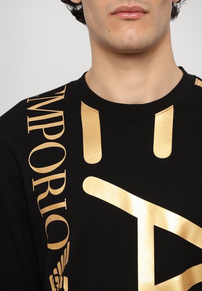 Sweatshirt en coton noir avec un grand texte doré imprimé et des éléments de design. Accents dorés notables et col rond.