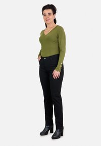 Top de punto de manga larga en verde oliva con escote en forma de V y detalles de botones en los puños, combinado con jeans ajustados negros y botas de tacón negras.