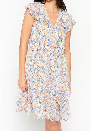 Femme portant une robe fleurie mi-longue avec des manches courtes à volants et une taille cintrée, dans des tons pastel bleu, orange et violet.