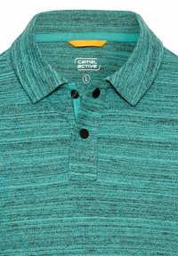 Turkusowa koszulka polo o teksturowanym dzianinie, z dwoma czarnymi guzikami i kołnierzykiem. Posiada kontrastowe turkusowe wykończenie i żółtą metkę wewnątrz.