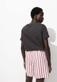 T-shirt noir à manches courtes et cropped associé à un short taille haute à rayures roses et blanches, affichant une coupe décontractée et des manches retroussées.