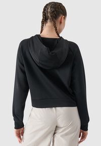 Felpa nera corta con cappuccio, maniche raglan e texture senza cuciture. Abbinata a pantaloni chiari e dai toni neutri.
