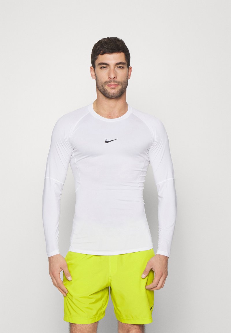 Hvid langærmet atletisk trøje med rund hals og sort Nike-logo. Båret med lys neongule shorts. Glat materiale og tætsiddende design.