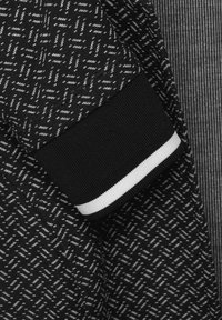 Detailní záběr na látku s černobílým vzorem a černým žebrovým manžetou se jednou bílou pruhou.