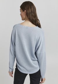 Maglione azzurro chiaro a maglia morbida con scollatura ampia e spalle drop. Texture morbida, orlo arrotondato, maniche lunghe e dettagli minimi.