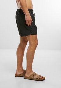Zwarte zwembroek met een elastische tailleband en trekkoord, met een zijzak en een gladde textuur. Draag met tan slip-on sandalen.