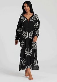 Czarna sukienka maxi z białym wzorem liści paproci, długimi rękawami, dekoltem w szpic, rozcięciami po bokach, lekkim materiałem i luźnym krojem.