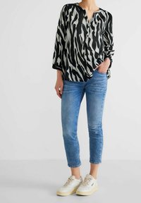 Blusa a maniche lunghe con motivo zebram in bianco e nero, con bottoni frontali, abbinata a jeans slim in denim blu e sneaker bianche.