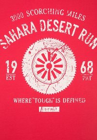 Rotes Baumwoll-T-Shirt mit weißem, abgenutztem Druck und dem Text: "3000 BRÜNSTENDE MEILEN SAHARA-WÜSTE LAUF" sowie einem kreisförmigen grafischen Design.