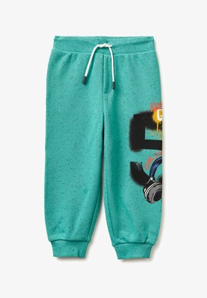 Pantalones jogger turquesa con manchas, cordón blanco y tobillos puño, con un gráfico negro de "5" y auriculares azules en una pierna.