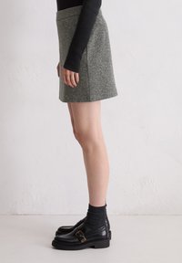Grauer, taillierter Minirock mit geradem Schnitt, kombiniert mit schwarzen Slippern und dunklen Socken. Der Rock verfügt über ein schlichtes Design mit minimalen Details.