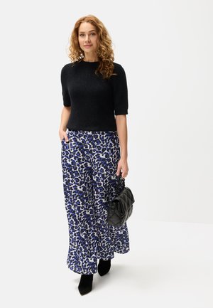 Black knit short-sleeve sweater paired with wide-leg blue and white floral print trousers. Model holds a quilted black handbag.