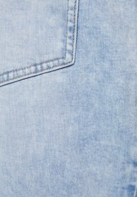 Světlá modrá denimbová látka s hladkou texturou, se čtvercovou kapsou a kontrastním prošíváním podél švů.