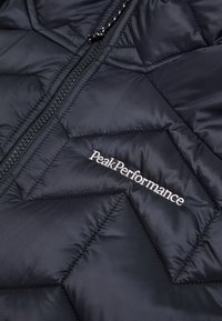 Mornarica podstavljena jakna s patentnim zatvaračem i bijelim "PeakPerformance" logom. Glatka tekstura s chevron uzorkom kroz cijelu jaknu.