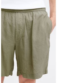 Olive green shorts with a textured pattern, featuring an elastic waist and side pockets. The fabric appears lightweight and breathable.