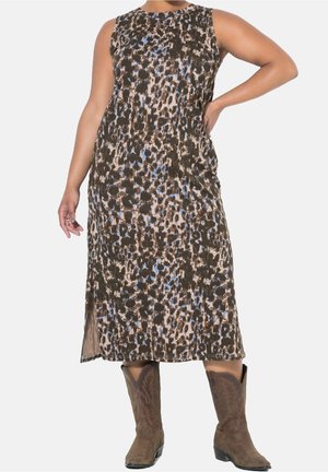 Femme portant une robe sans manches, longueur mollet, imprimé animalier, associée à des bottes de cow-boy marron brodées, debout avec une main sur la hanche.
