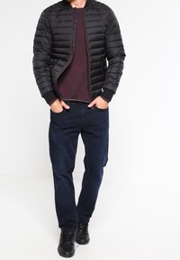 Musta tikattu bombertakki, viininpunainen paita, tummansiniset housut, mustat kengät. Takissa on vetoketjulla suljettava etuosa ja resorireunukset hihoissa.