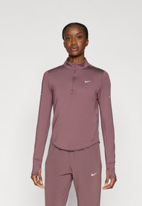 Μπλούζα για αθλητισμό με μακριά μανίκια, σε λεβαντίνι απόχρωση, με ψηλό γιακά και φερμουάρ μέχρι τη μέση. Φέρει μικρό λευκό λογότυπο Nike στο στήθος. Λείο, ελαφρύ ύφασμα.