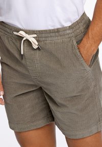 Pantalones cortos de pana en verde oliva, con una cintura ajustable con cordones de color crema, textura estriada y bolsillos laterales.